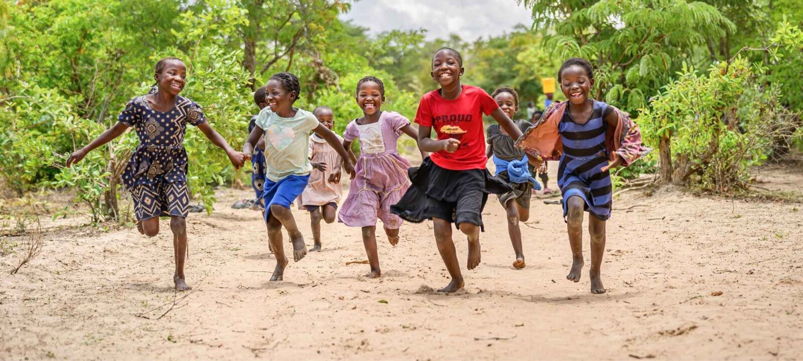 Girls hold hands and run down the road in Muchila AP, Zambia, where a World VIsion drilling crew is at work drilling a borehole to bring them clean water.