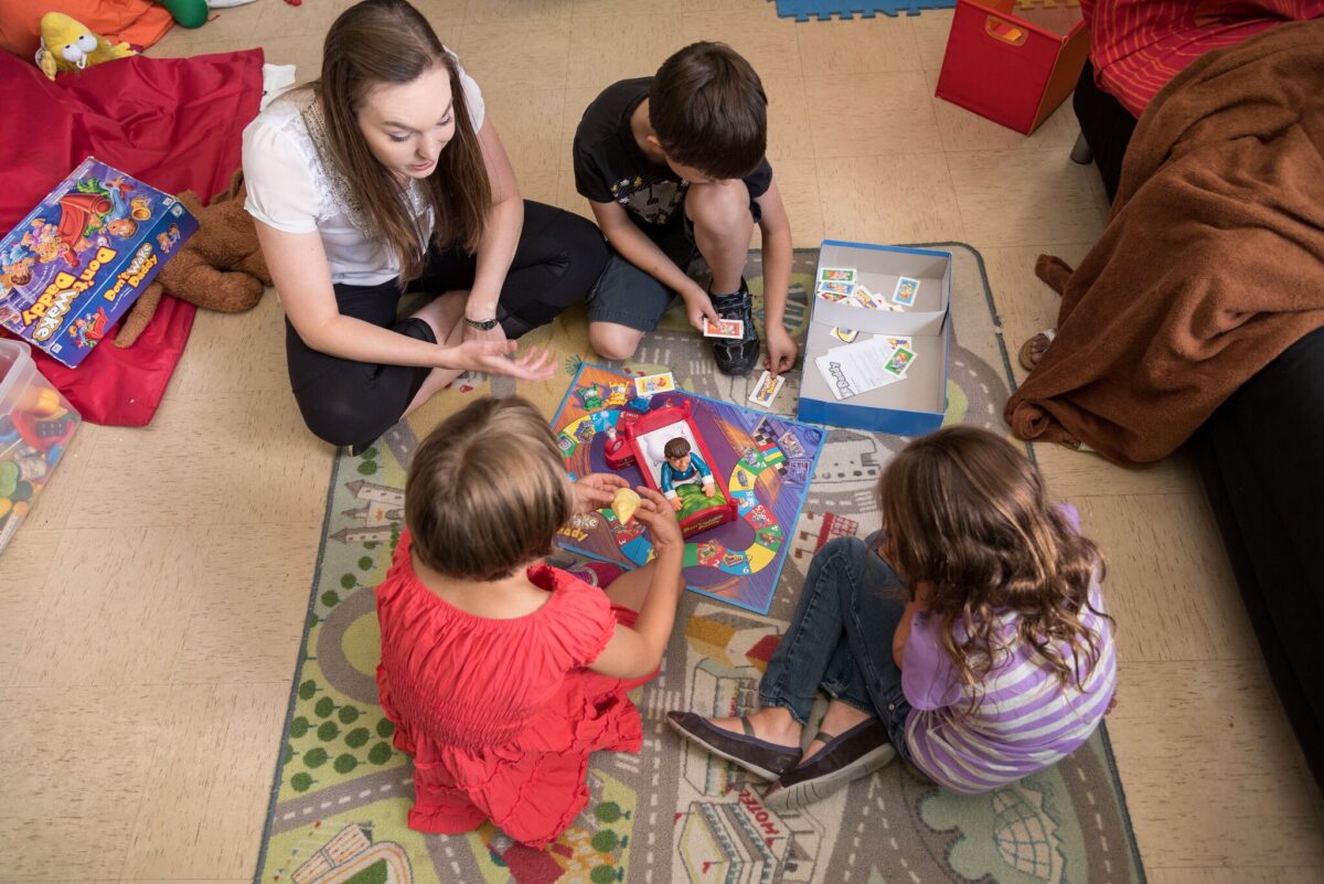 Autism instructor and three children playing boardgame on the floor