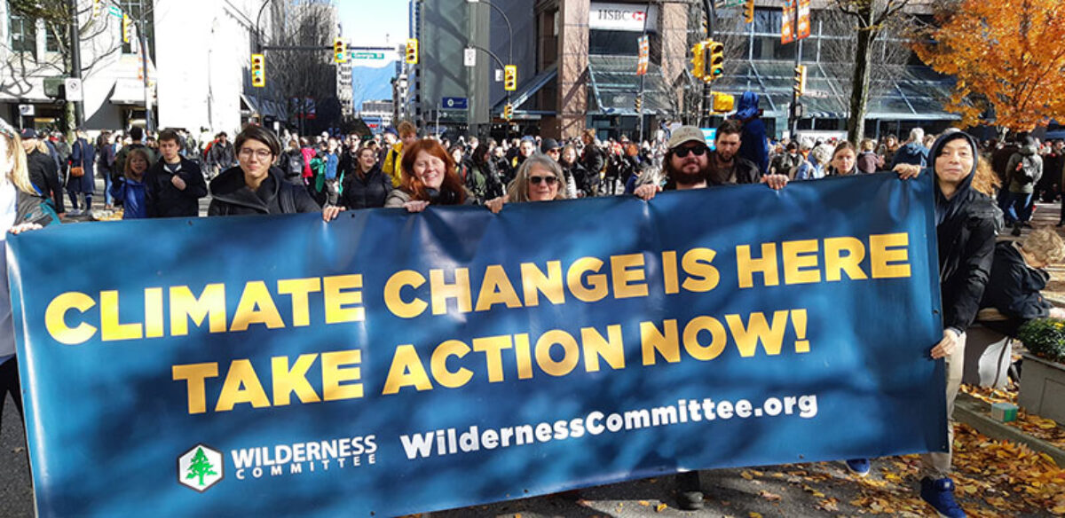 A crowd of people, with those in the fore holding a sign that says 