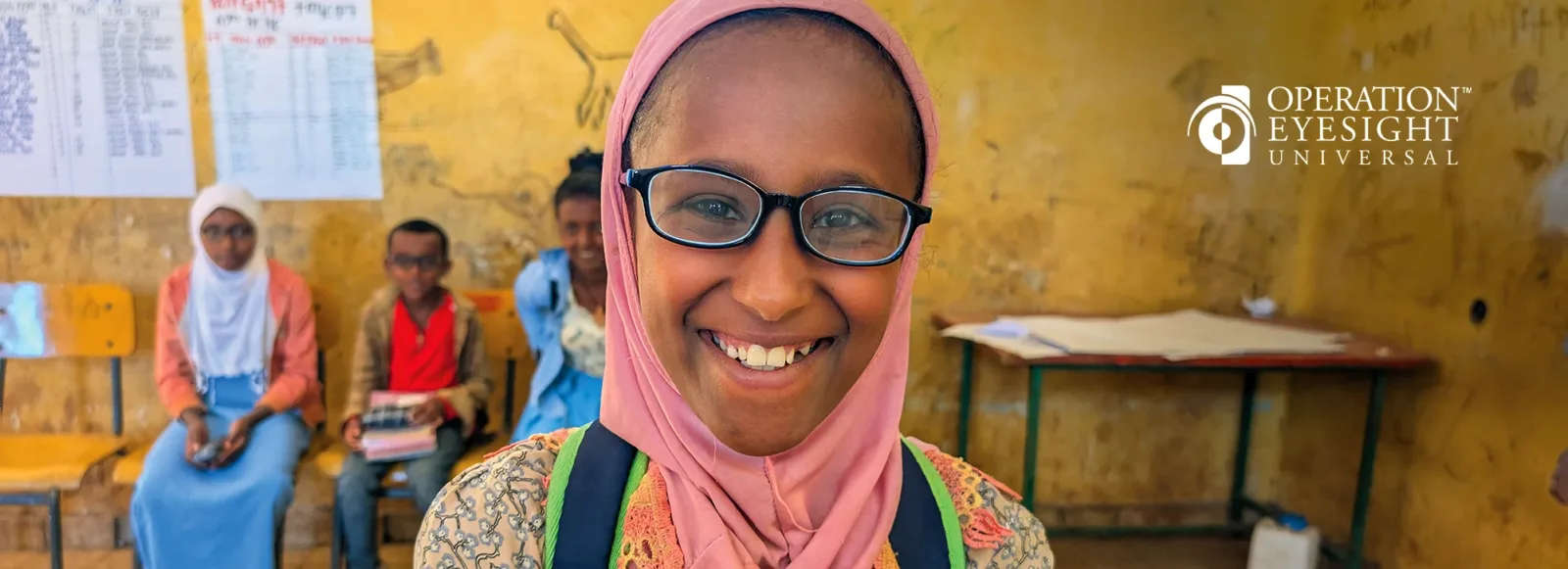 A girl smiles at the camera. She wears a pair of prescription glasses.