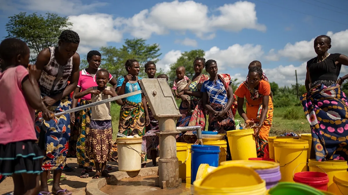 A group of women are gathered around a borehole, collecting water in buckets.