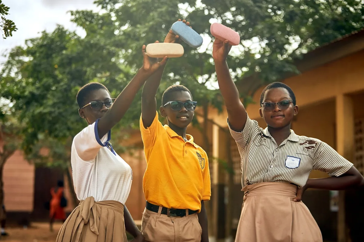 Three teenagers hold up cases for their new eyeglasses, which they are all wearing. They are all in school uniforms.