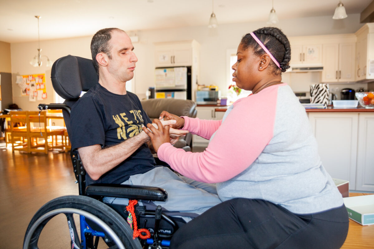 Man in a wheelchair is using sign language to communicate with his intervenor
