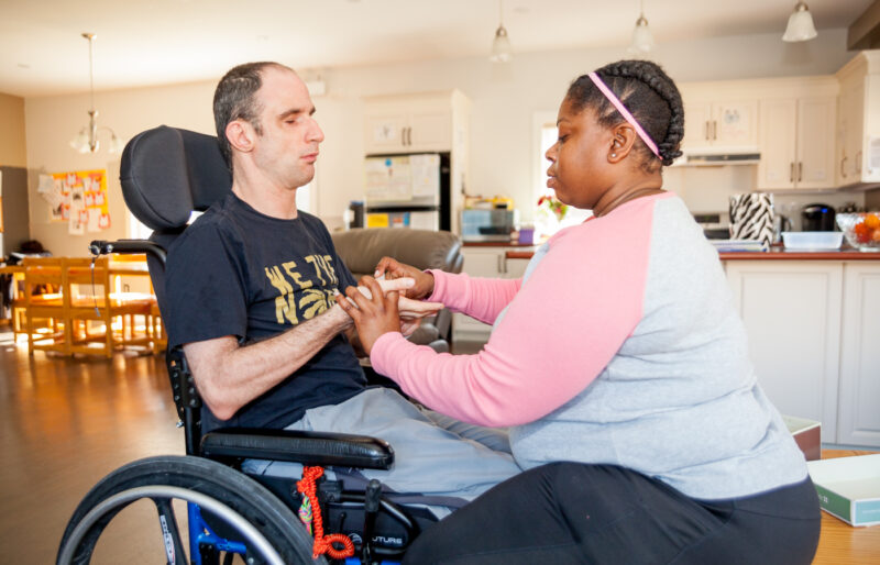 Man in a wheelchair is using sign language to communicate with his intervenor