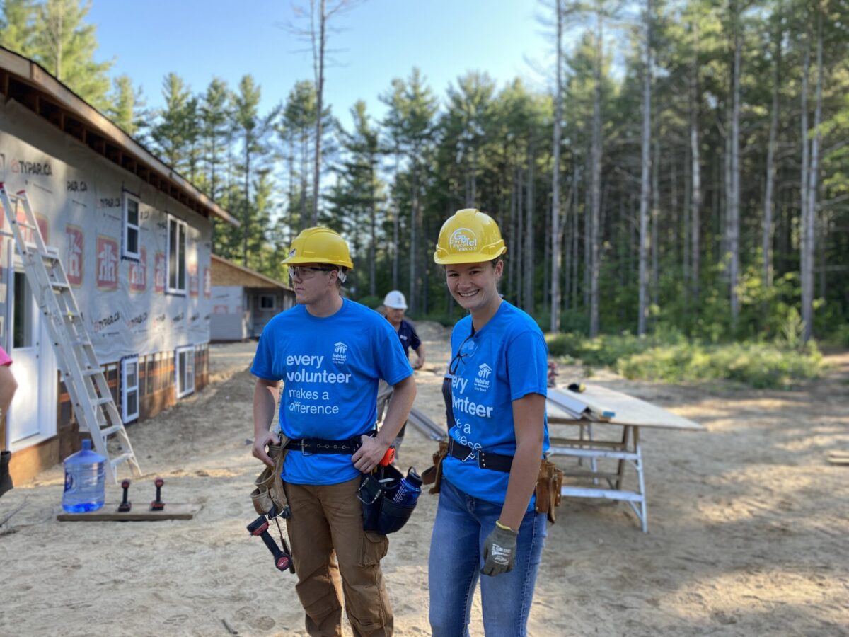 Two people wearing construction gear while helping build a house for Habitat for Humanity