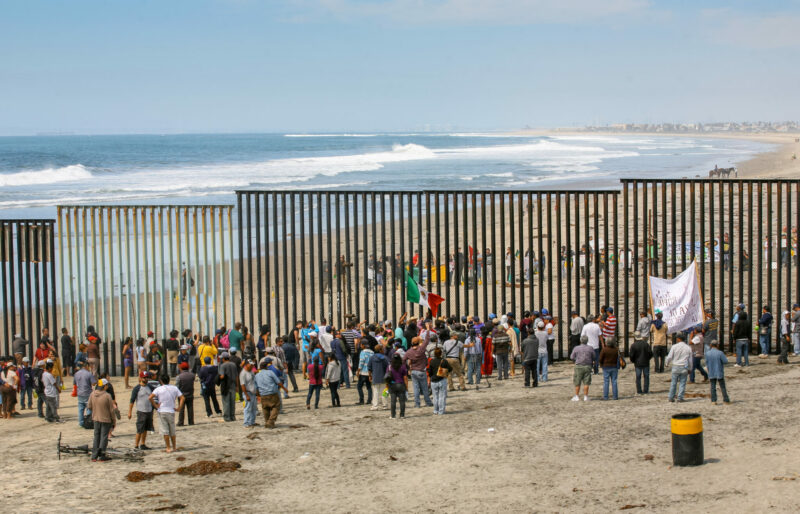 Dozens of migrants and workers on the sides of the US-Mexico border wall in Tijuana Beach.