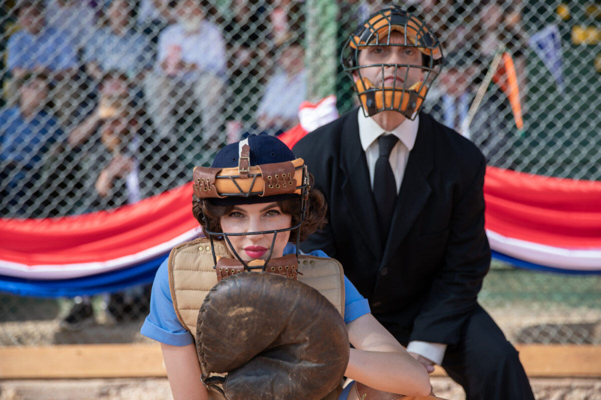 A female baseball catcher crouches in front of an umpire during a game.
