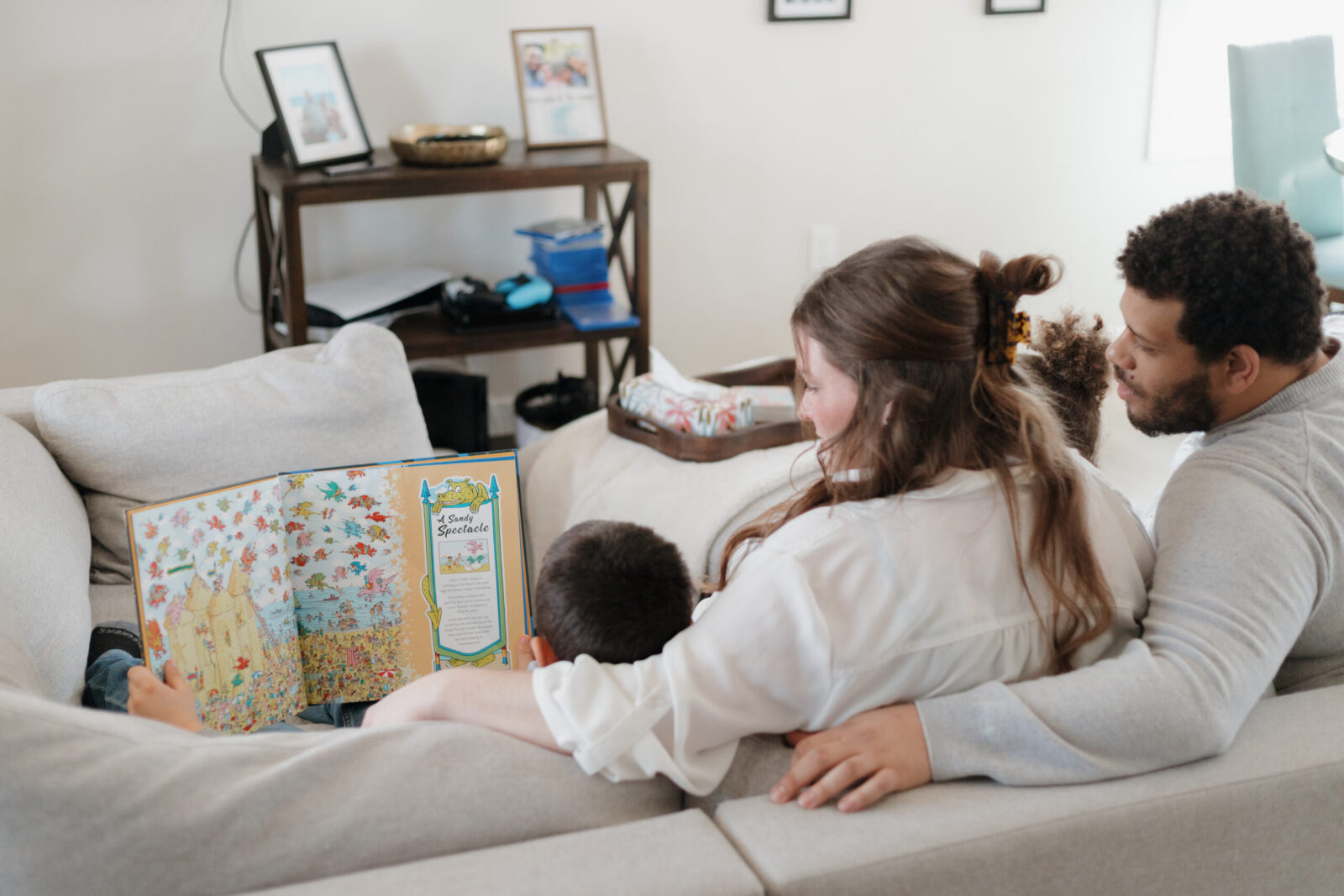 A family sitting on a couch with their backs to the camera reading a book in their living room