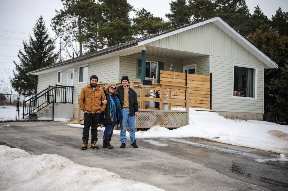 Family of mom and two boys standing in front of their house outside in the winter