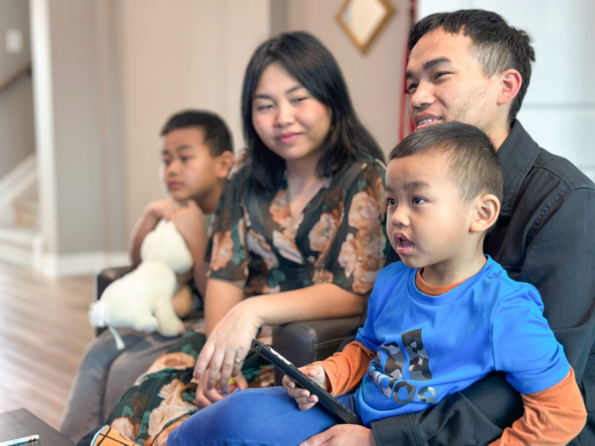 Family, with two parents and two children sitting on a couch watching television, while looks towards one of her children.