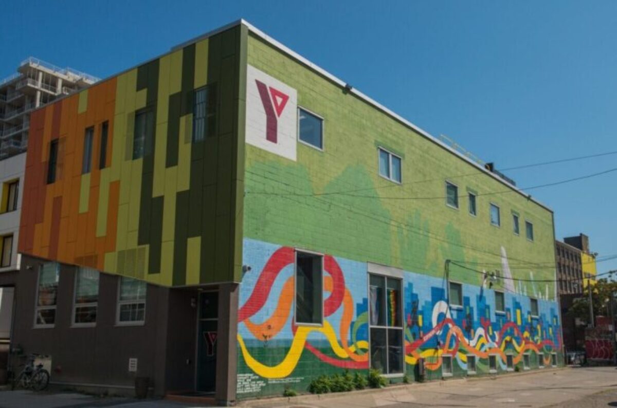 Corner of a downtown 3 story building painted green with a mural in bright colours